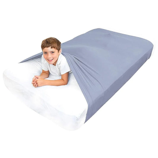 Child lying on a bed with a fitted gray compression blanket for special needs covering the mattress