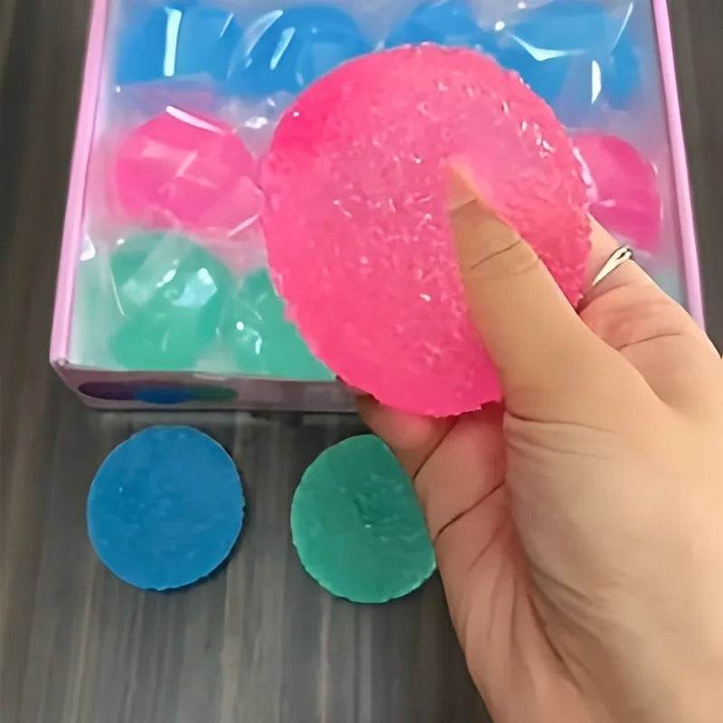 Hand squeezing a pink textured stress ball with a container of colorful stress balls in the background.